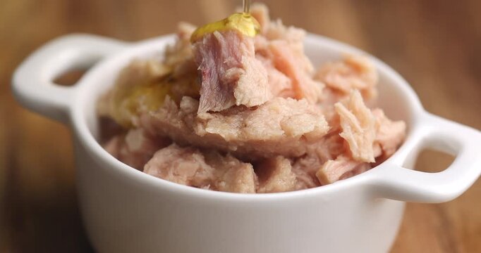 Close up of a hand pouring oil onto tuna in a white ceramic dish, emphasizing flavor, freshness, protein-rich seafood, and healthy meal preparation