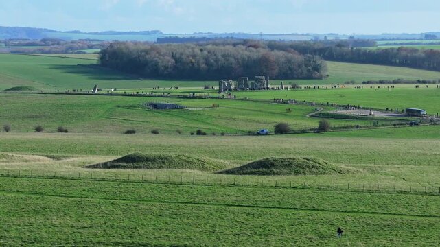Telephoto aerial tracking shot of Burial mounds in foreground and Stonehenge in the distance