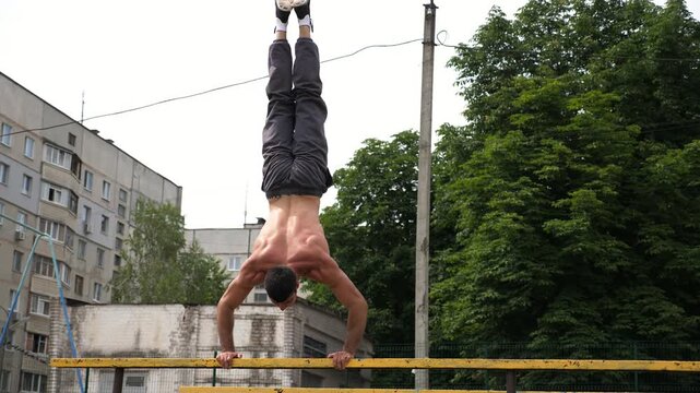 Sportsman performing dynamic workout routine, transitioning from push-up position to handstand on parallel bars, showcasing strength and balance in an outdoor training environment