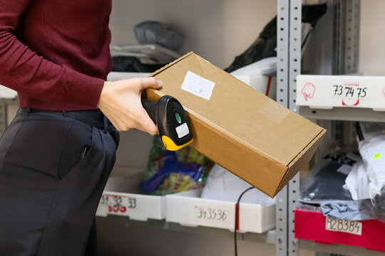 Worker scanning package barcode in storage area. Close-up of hand holding scanner to brown box label on shelf with various packages