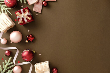 Festive Christmas frame on a dark brown background with red and white gifts, pink and red baubles, velvety ribbon, and snowy fir branches. Luxury holiday flat lay with copy space.