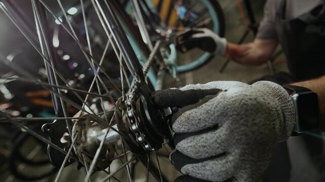 Unrecognizable repairman wearing gloves checking bicycle drivetrain system while fixing it in workshop