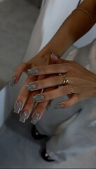 A stylish close-up of a woman's hands showcasing long square-shaped nails painted with a glossy trendy grey gel polish. The image suggests fashion beauty and professional manicure services.