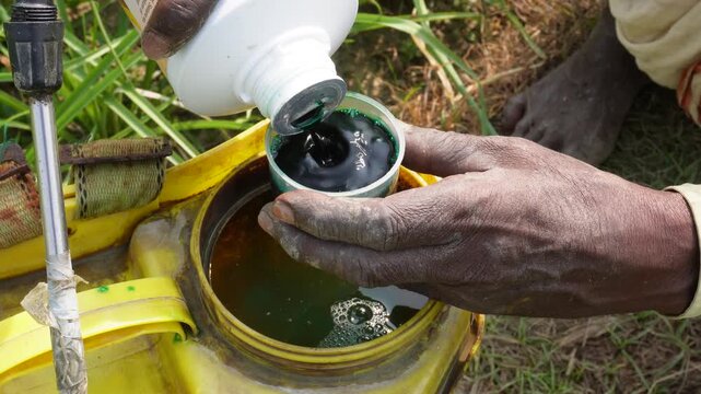 Farmers mixing a dark liquid pesticide yellow container filled with water for preparing agricultural sprays