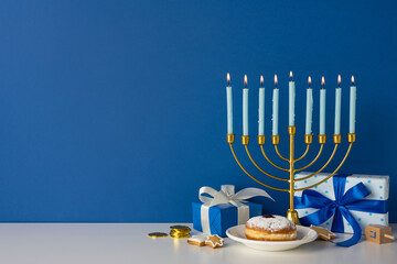A golden menorah with lit candles sits beside blue gift boxes, a plate with a pastry, coins, and...