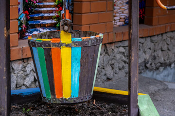 A bucket near the well made of wood of different colors.