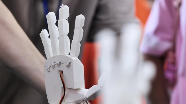 A person controls an artificial robotic arm via wires on their hand.