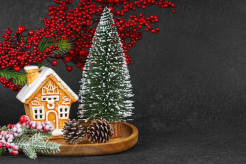 Gingerbread style ceramic Christmas house surrounded by pine cones, holly berries, and frosted...