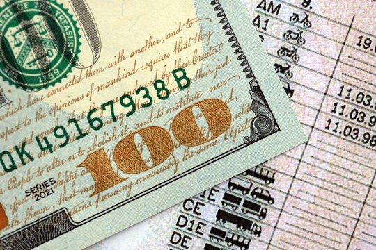 Hundred dollar bill on US driver license close up. Concept of driving lessons or automobile taxpaying