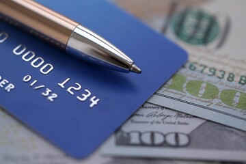 One hundred US dollar bills and silver pen with blue credit card close up. Concept of business calculating and accounting in United States