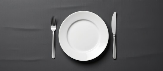 A minimalist setting featuring a plate, fork, and knife on a dark surface.