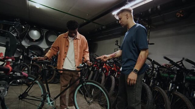 Young Caucasian seller working with young Black male customer in shop, recommending him one of bicycles