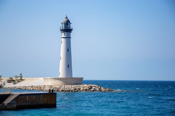 A sea lighthouse against the background of the blue sky and the blue sea. Landmark beacon for ships
