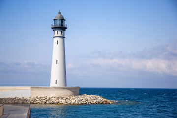 A sea lighthouse against the background of the blue sky and the blue sea. Landmark beacon for ships