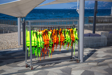 Green and orange Life jackets hanging on a hanger in the port near the boarding of water attractions with the sea in the background