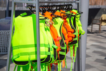Green and orange Life jackets hanging on a hanger in the port near the boarding of water rides