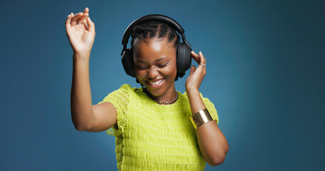 Headphones, happy and black woman in studio with music, radio or song for rhythm and energy. Dancing, audio tech and African person listening to album for groove entertainment by blue background.