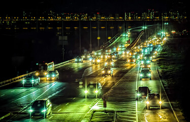 Highway cars at night with light trails. Traffic jam before turning onto a bridge. A city interchange street. A multi-lane thoroughfare.