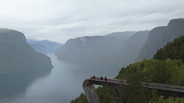 Drone view of Stegastein platform extending over fjord cliffs with tourists, Norway