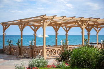 View of the summer terrace of the restaurant on the sea coast. Beautiful blue sea in the background, a passing ship, a cafe in a wooden style with eco-friendly furniture