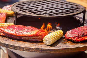A piece of meat and ears of corn are grilled. Barbecue outside in a local cafe on an open fire