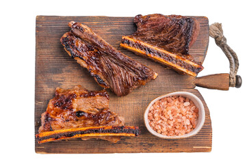 Gourmet grilled beef short ribs served on a rustic wooden board with a bowl of pink Himalayan salt. Clean white background.