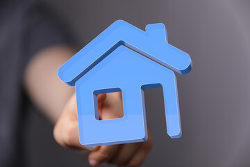 Hand holding a blue house icon, representing real estate, mortgage, and home ownership. Perfect for illustrating concepts of housing, property i