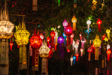 Naklejka premium Vibrant traditional Lanna lanterns illuminate the night, hanging amidst lush foliage. This festive display captures the enchanting atmosphere of a cultural celebration, possibly during Thailand's Yi