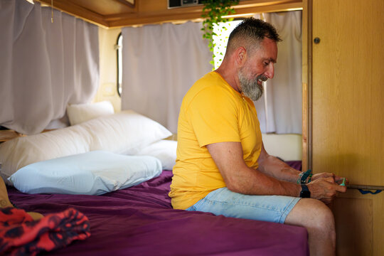 Smiling bearded man enjoying digital entertainment on smartphone inside camper van during leisure trip