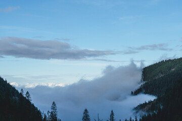 low clouds approaching foggy morning in Carpathians autumn landscape with forest woods and blue sky above 