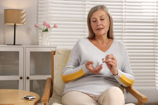 Diabetes. Woman checking blood sugar level with lancet pen on armchair at home - Powered by Adobe