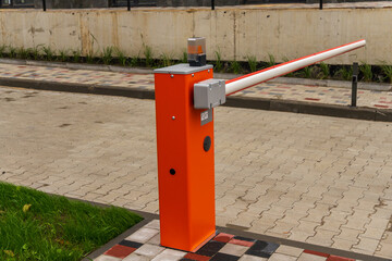 Bright orange crossbar barrier stands by a paved parking lot, designed to manage vehicle entry and exit efficiently