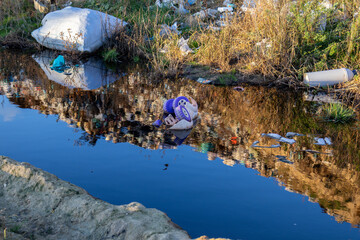 Dark water polluted with garbage reflects the surrounding debris in a neglected area, highlighting serious environmental concerns