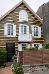 Façade avec fenêtres et petit balcon blancs d'une maison moderne, recouverte d'un bardage verni de couleurs brune, jaune et verte.