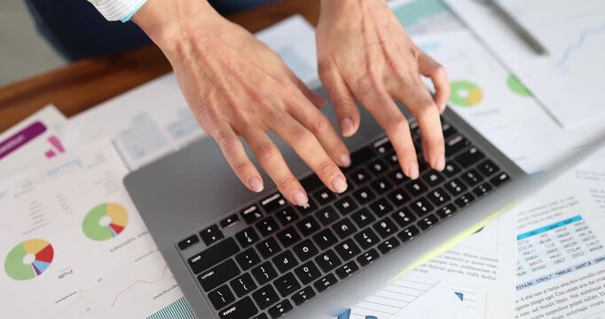 Woman office worker types on modern laptop keyboard focusing carefully on text appearing on screen. Employee works at computer pressing keys