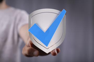 Hand holding a shield with a blue checkmark, symbolizing protection, security, and approval....