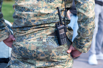 A military man is standing on the street in a camouflage uniform and with a walkie-talkie on his...
