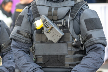 A fighter is standing outside in a bulletproof vest with a taser mounted on the front panel.