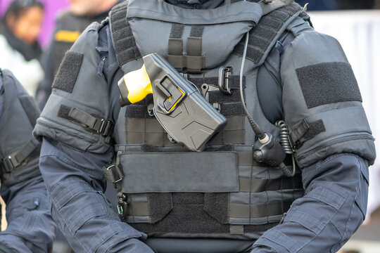 A fighter is standing outside in a bulletproof vest with a taser mounted on the front panel.