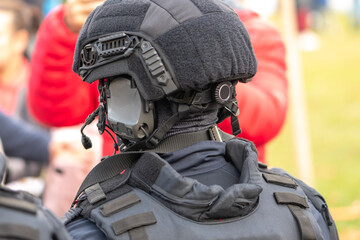 A protective helmet with a headset is worn by a policeman standing at an open city event.