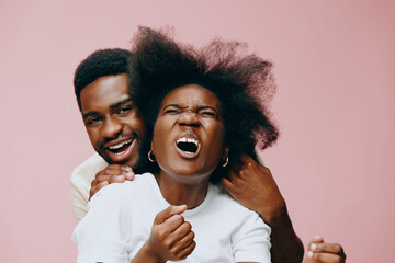 Joyful African couple expressing excitement on a pastel pink background, showcasing natural hair and vibrant emotions in casual attire
