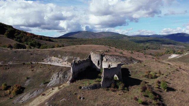 Aerial drone footage of the medieval Bjelaj Fortress near Bosanski Petrovac, Bosnia and Herzegovina. The ancient ruins stand atop a scenic hill surrounded by rugged mountains and natural autumn colors