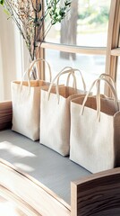 Three natural canvas tote bags are arranged on a wooden bench, bathed in soft sunlight from a nearby window, with a vase of dried flowers in the background.