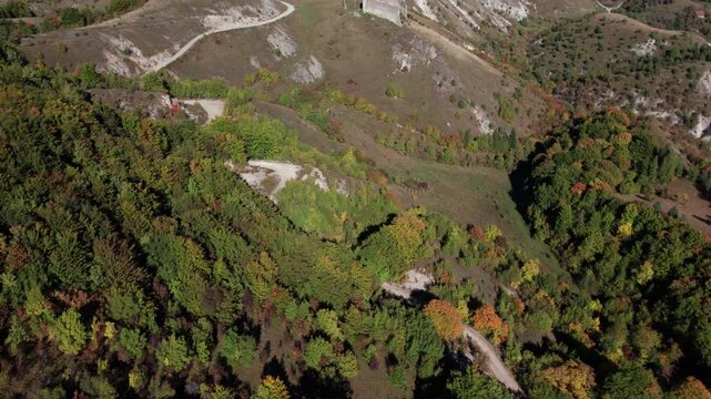 Aerial drone footage of Bjelaj Fortress near Bosanski Petrovac, Bosnia and Herzegovina. The medieval ruins sit atop a steep hill surrounded by winding mountain roads, forests, and the scenic landscape