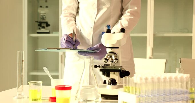 Woman laboratory assistant records test results in document. Female lab worker writes findings from experiment into laboratory report on clipboard
