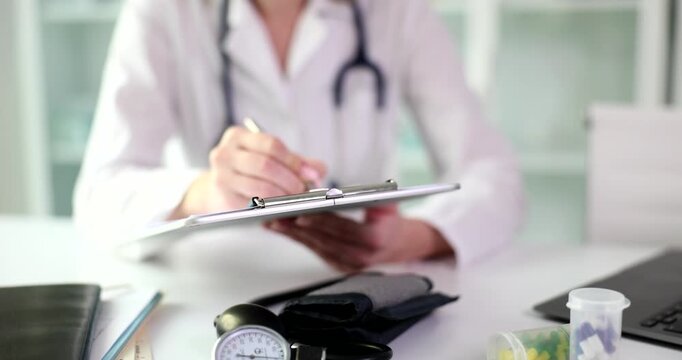Woman doctor carefully records results of patient examination on clipboard. Physician in white coat writes prescription for necessary medication