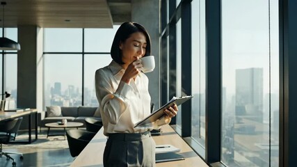 Asian businesswoman standing by a large window in a high-rise corporate office, enjoying a hot beverage while reviewing important business documents with a city view backdrop - Powered by Adobe