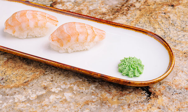 Fresh shrimp sushi served on a long white plate with wasabi