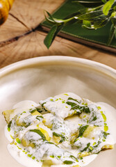 Freshly made ravioli filled with seasonal ingredients is plated with a rich cream sauce and garnished with vibrant greens. This dish showcases culinary skill and flavor.