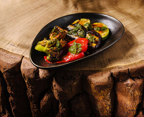 Grilled vegetables served on a sleek black plate with wooden background